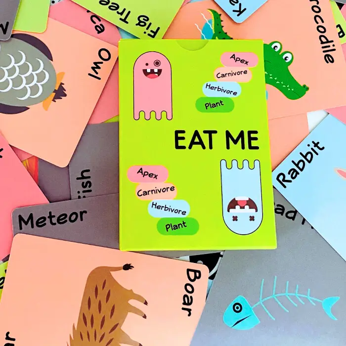 The EAT ME box standing among scattered animal cards.