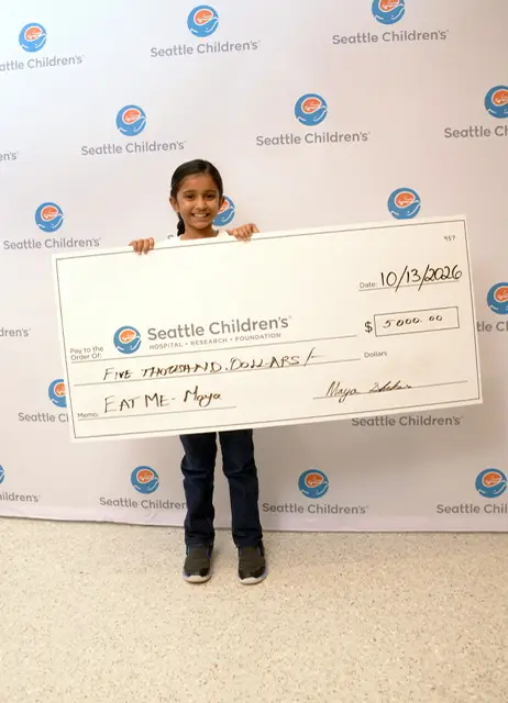 Maya holding a giant $5,000 check made out to Seattle Children's Hospital