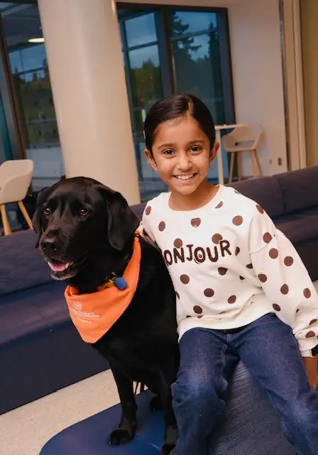 Maya hugging a friendly black therapy dog at the hospital