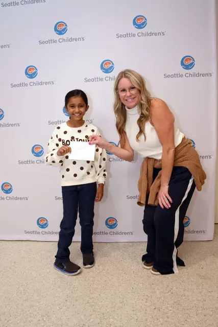 Maya handing the gift to a Seattle Children's staff member